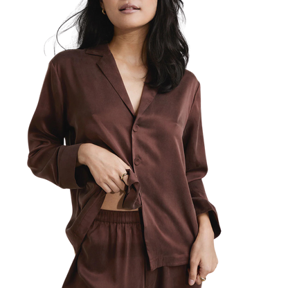image of woman wearing the lunya washable silk pajamas in dozing umber holding up the shirt to see the elastic band 
