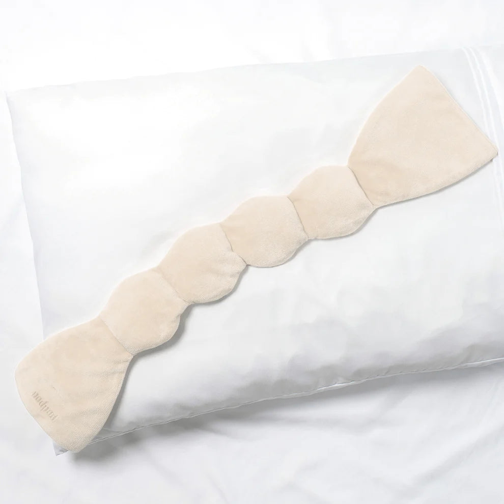 the Nodpod Sleep Mask in bone laying on a pillow sold at heaven on earth so you don&