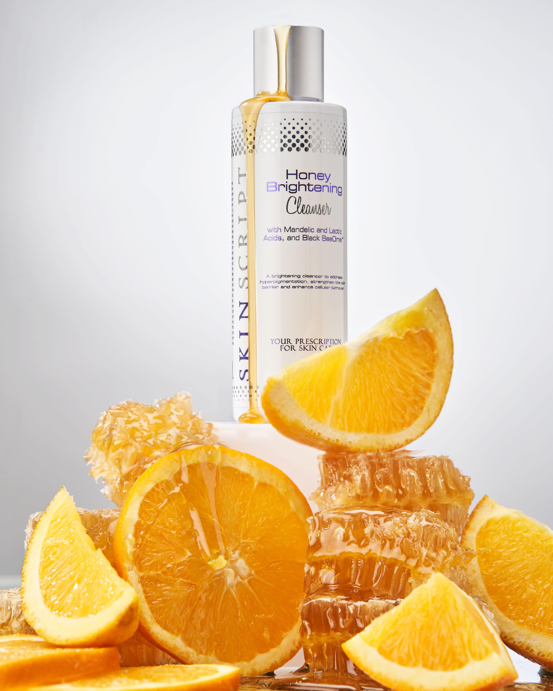 Skin Script Honey Brightening Cleanser with honeycomb and orange slices on a light gray background