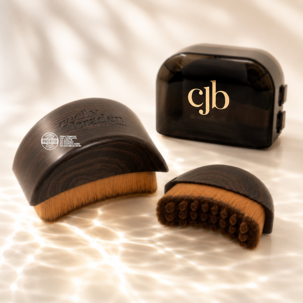 two lymphatic brush tools with light brown bristles are arranged on a warm white surface with soft leaf shadows. one large brush is shown , one small brush is shown and one large case is shown with the logo in gold 'cjb' logo on the front, and one 
