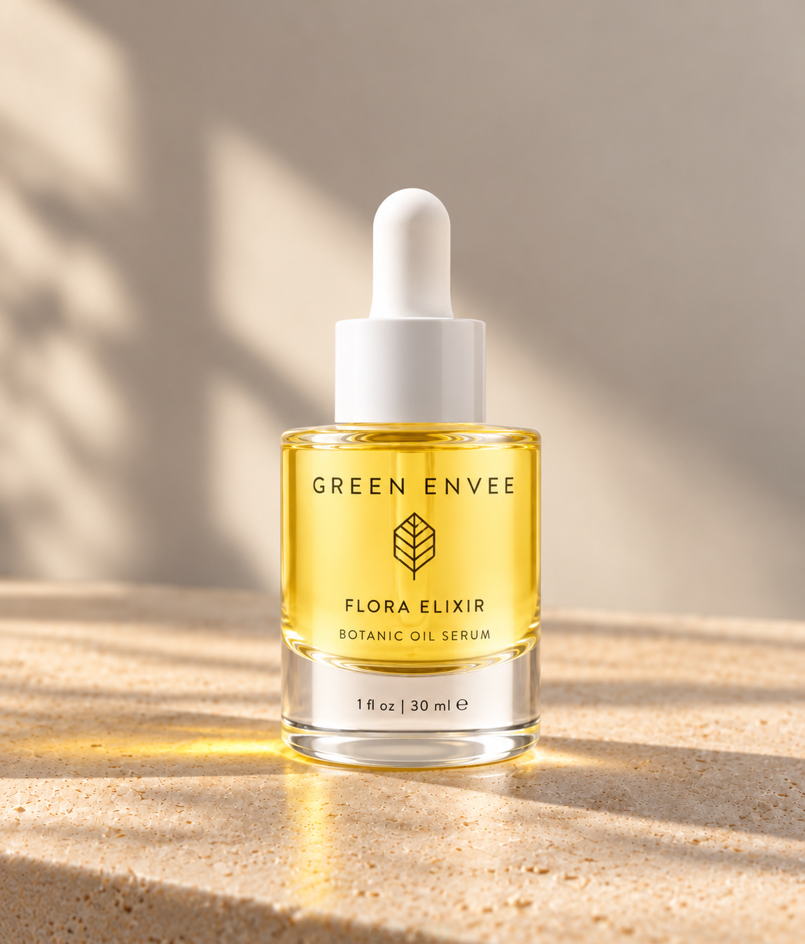 A bottle of GREEN ENVEE Flora Elixir Botanic Oil Serum with a white dropper cap, filled with golden yellow oil, set on a textured beige stone surface with warm sunlight and leaf shadows.