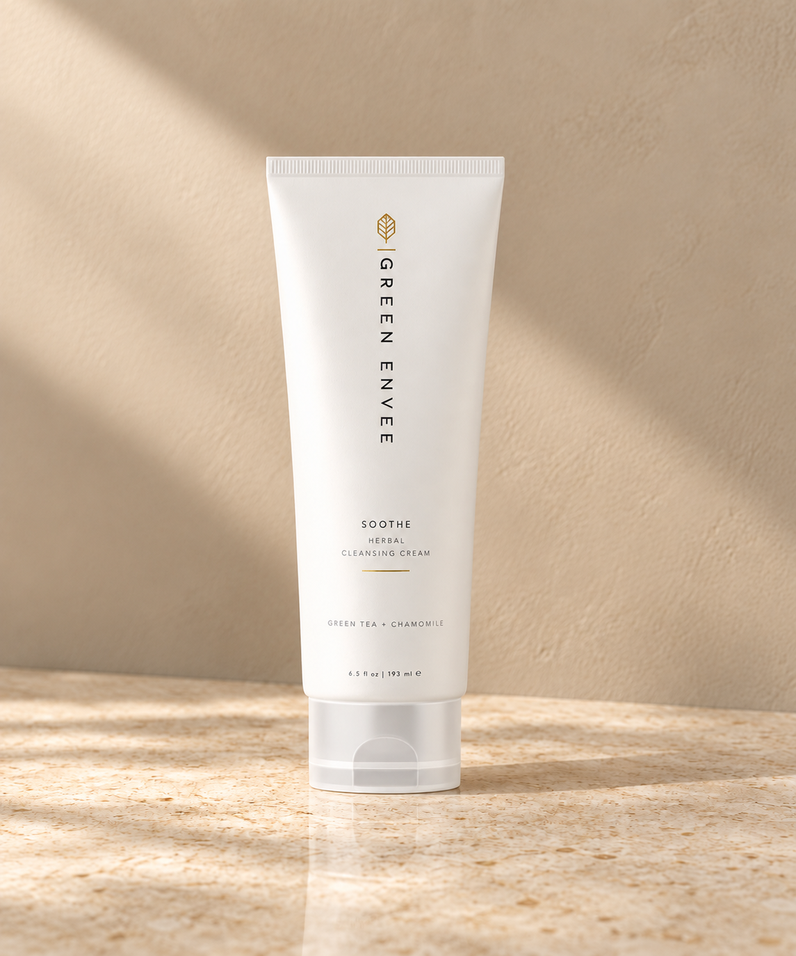 a squeeze tube bottle of Green Envee Cleansing Cream on a beige marble backdrop with a light casting on it 