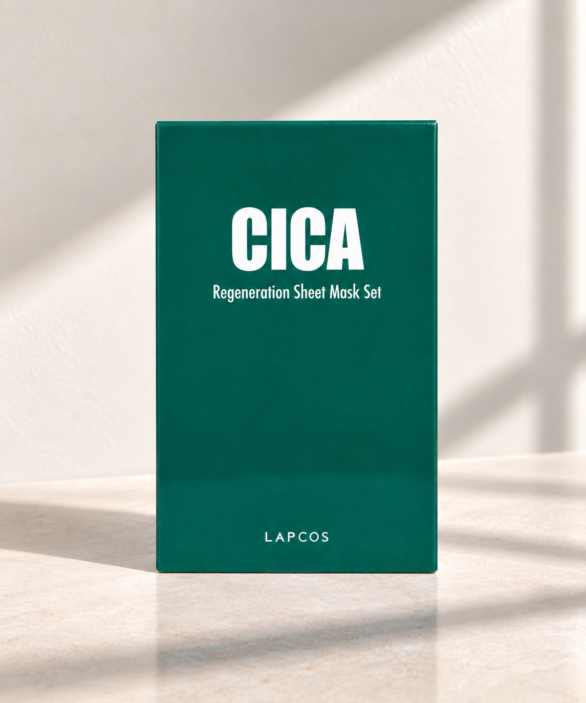 A tall rectangular dark teal-green box standing upright on a light stone surface, with white text reading 'CICA Regeneration Sheet Mask Set' and 'LAPCOS' near the bottom. 