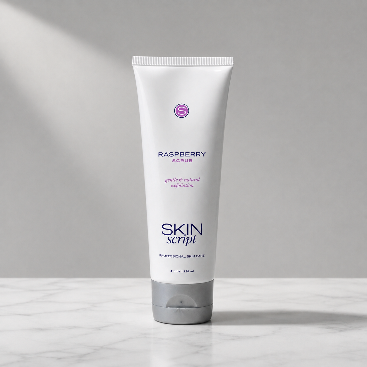 A white squeeze tube of Skin Script Raspberry Scrub standing upright on a light marble surface against a gray background with soft diagonal shadows.